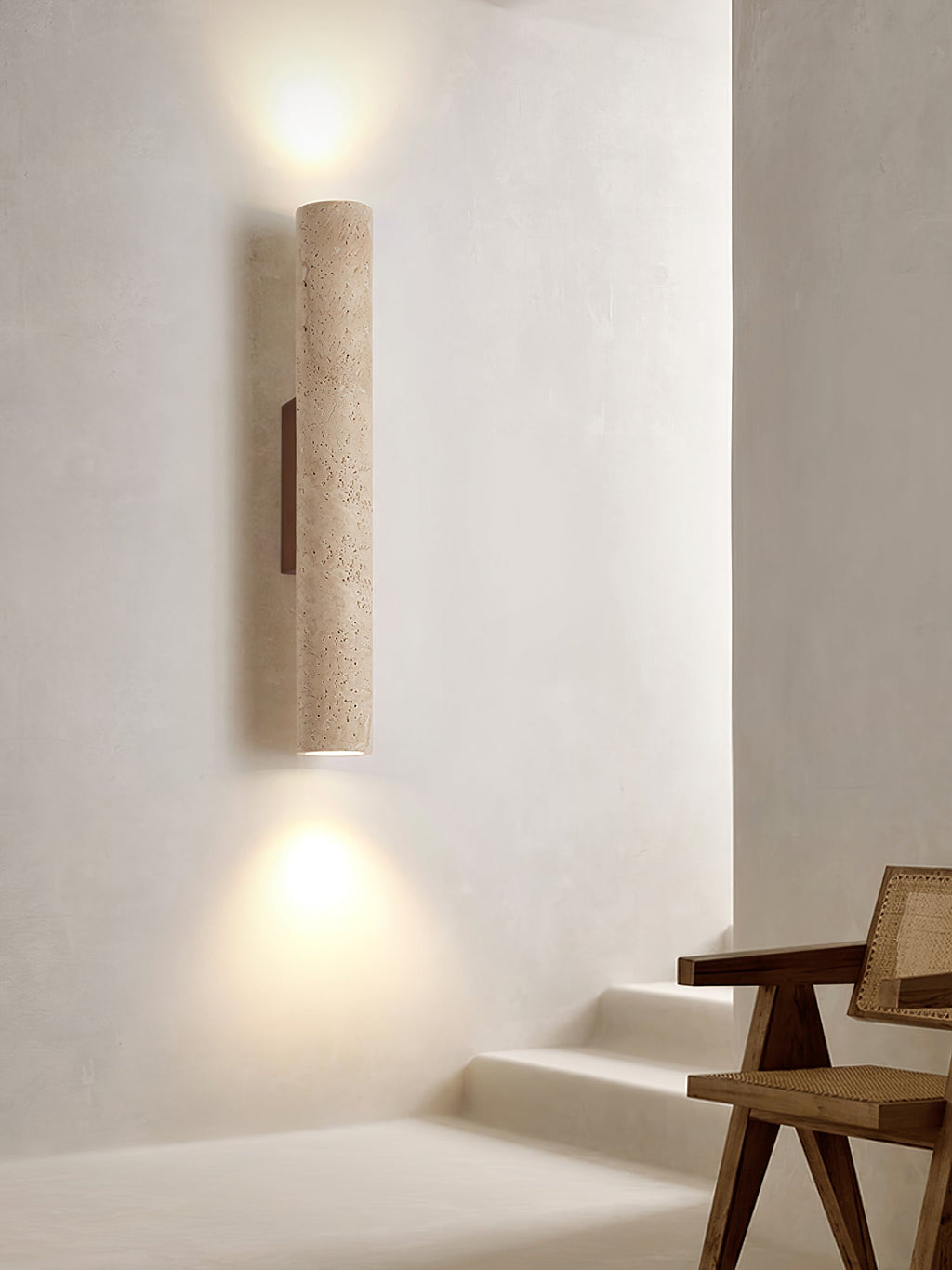 A rattan chair sits in a stairwell corner beneath this Clérachic wall light, lit.