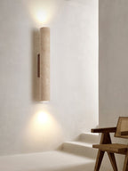 A rattan chair sits in a stairwell corner beneath this Clérachic wall light, lit.