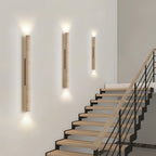 Three of this Clérachic wall light run lit up a staircase wall beside wood and metal steps.