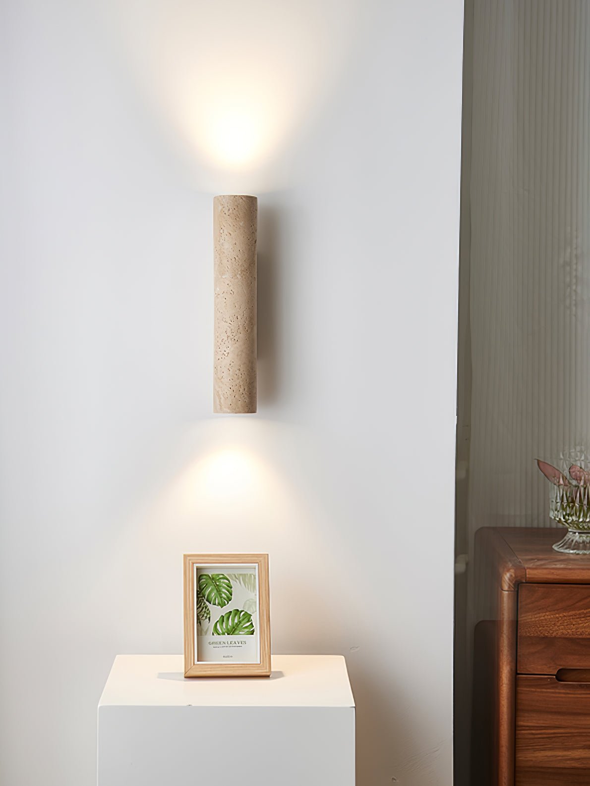 This Clérachic wall light glows above a plinth holding a small framed photo in a minimalist corner.