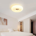 Clérachic ceiling light mounted flush in a cream bedroom, glowing above a bed with a pom-pom cushion and abstract art.