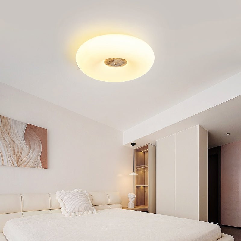 Clérachic ceiling light mounted flush in a cream bedroom, glowing above a bed with a pom-pom cushion and abstract art.