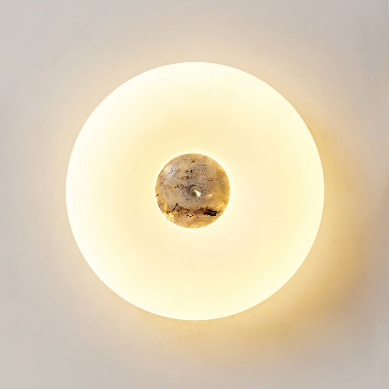 Close-up of a lit Clérachic ceiling light with a dark, marbled stone centre glowing warmly against a plain wall.
