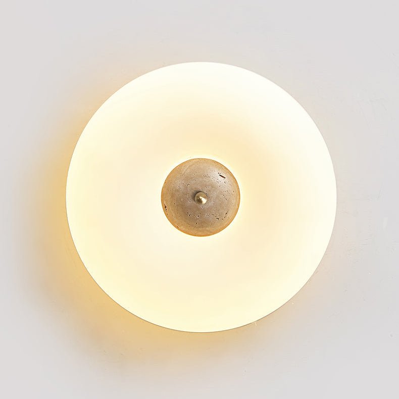 Close-up of a lit Clérachic ceiling light with a paler, plain stone centre, its warm ring glowing on a grey wall.