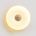 Close-up of a lit Clérachic ceiling light with a paler, plain stone centre, its warm ring glowing on a grey wall.