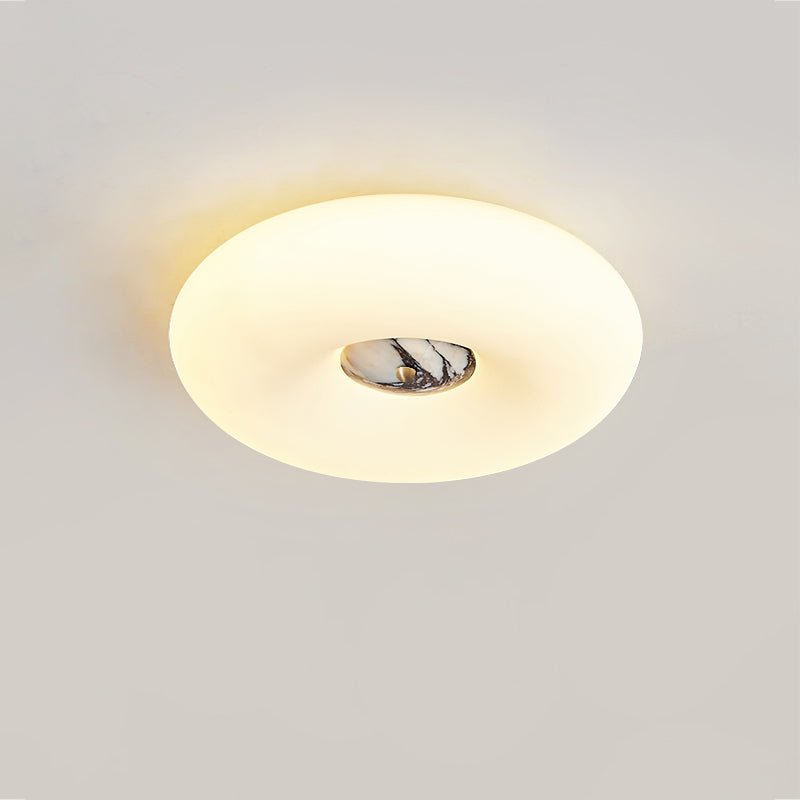 Clérachic ceiling light seen from a low angle, its oval glow and dark marbled stone centre lit against a grey wall.