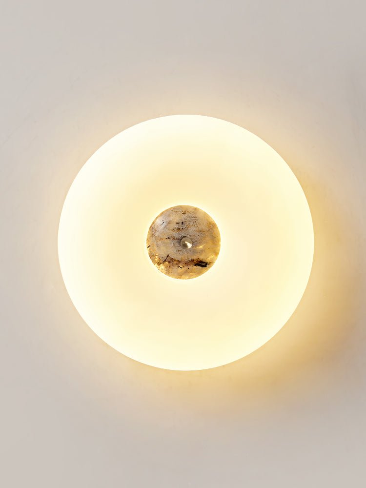 Clérachic ceiling light in a tall crop against a plain wall, its dark grey marbled stone centre lit warmly.