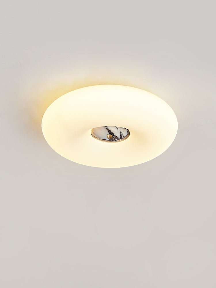 Clérachic ceiling light in a low oval crop, its black-and-white marbled stone centre lit against a plain wall.