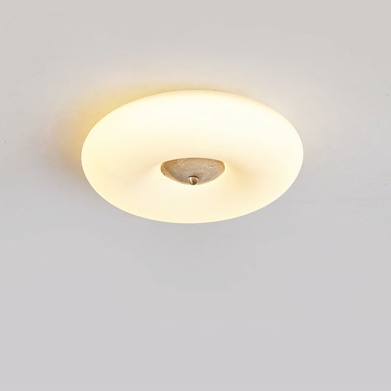 Clérachic ceiling light seen almost edge-on, flattened into a wide ellipse, its small pale stone centre lit softly.