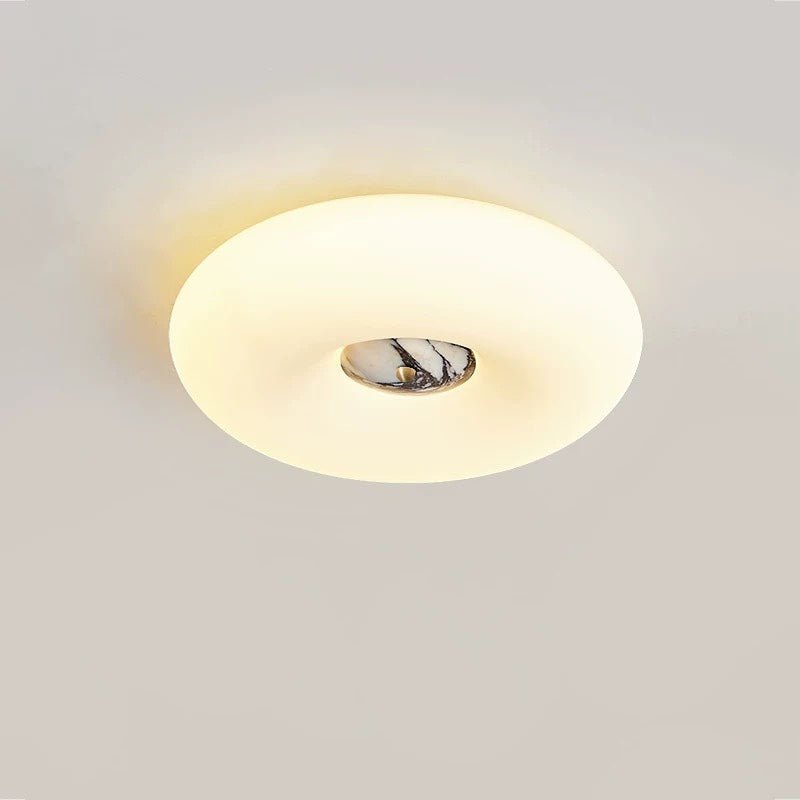 Clérachic ceiling light in a wide oval crop, its dark grey marbled stone centre glowing on a plain grey backdrop.