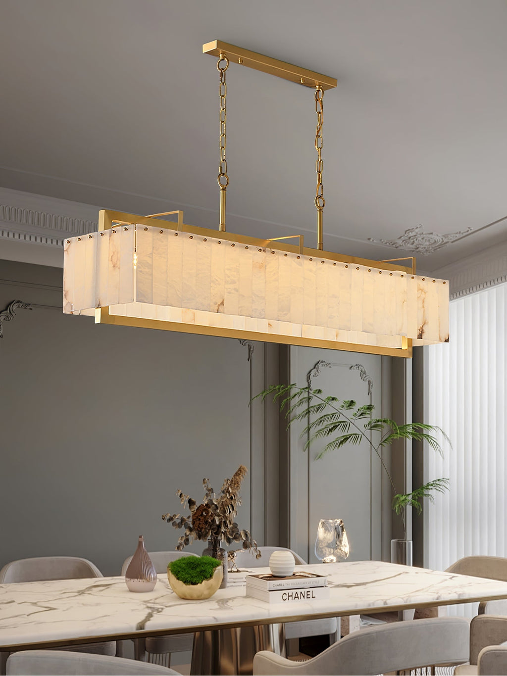 Lit over a marble dining table with dried stems and books, a palm to the right.