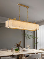 Lit over a marble dining table with dried stems and books, a palm to the right.