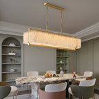 The chandelier lit above a dining table in a green-grey room with arched display shelving.