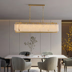 Lit above a marble dining table in a grey panelled room, yellow forsythia branches alongside.