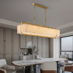 The chandelier lit over a dining table in a grey room, tall window and cabinetry behind.