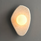 The beige stone wall light from Clérachic switched on, its white orb glowing against a grey studio backdrop.