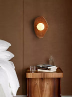 This Clérachic wall light in coral-red marble glows above a walnut nightstand with books and pillows in a bedroom.