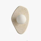 Unlit beige stone wall light from Clérachic on a white studio background, showing its freeform carved shape.