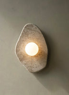 The beige stone wall light from Clérachic glowing on a sage-grey wall, casting a soft shadow beneath it.