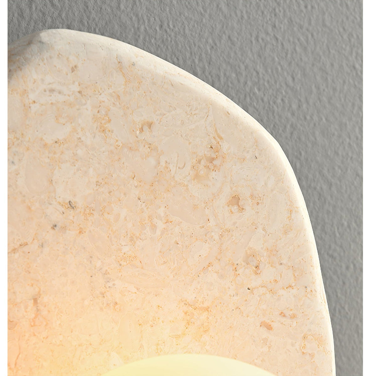 Extreme close-up of the beige stone's mottled texture and carved edge on this Clérachic wall light.