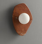 Wide view of the coral-red marble wall light from Clérachic, lit, on a grey studio wall with the orb centred low.