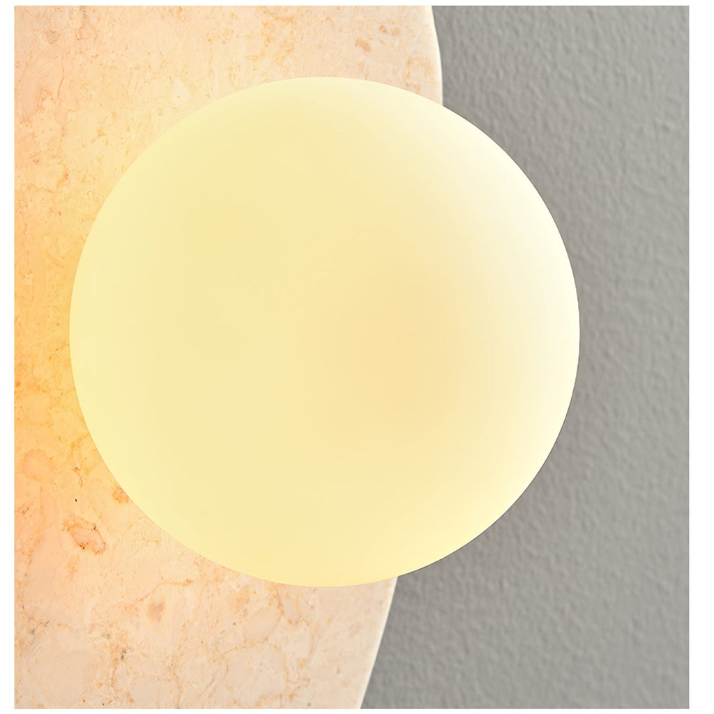Close-up of the lit white glass orb set into the beige stone body of this Clérachic wall light.