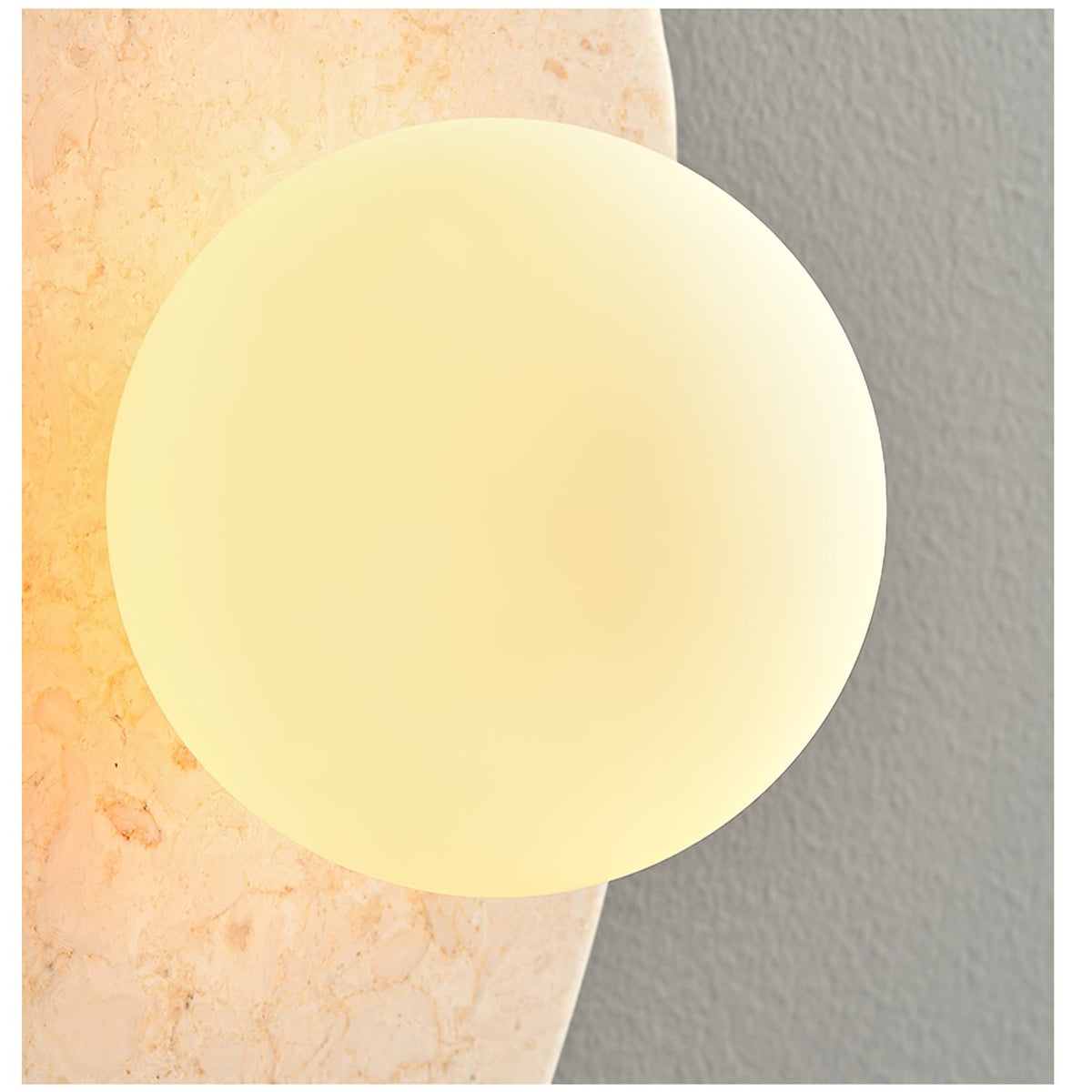 Close-up of the lit white glass orb set into the beige stone body of this Clérachic wall light.