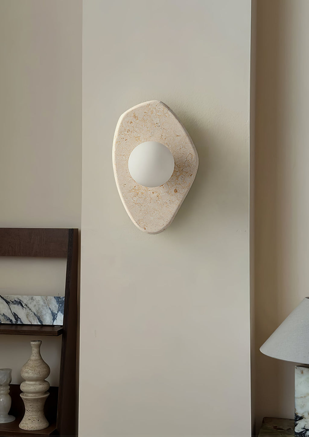 The Clérachic stone wall light mounted on a hallway pillar, glowing beside a low console with vases and a table lamp.