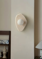 The Clérachic stone wall light mounted on a hallway pillar, glowing beside a low console with vases and a table lamp.