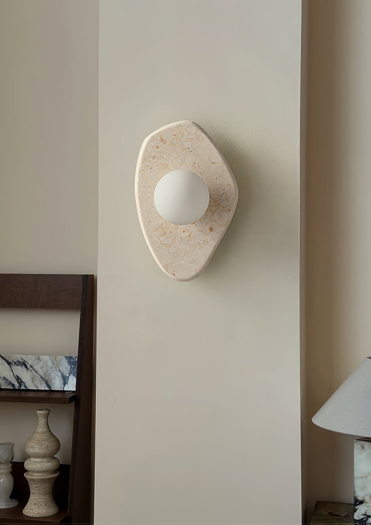 The Clérachic stone wall light mounted on a hallway pillar, glowing beside a low console with vases and a table lamp.