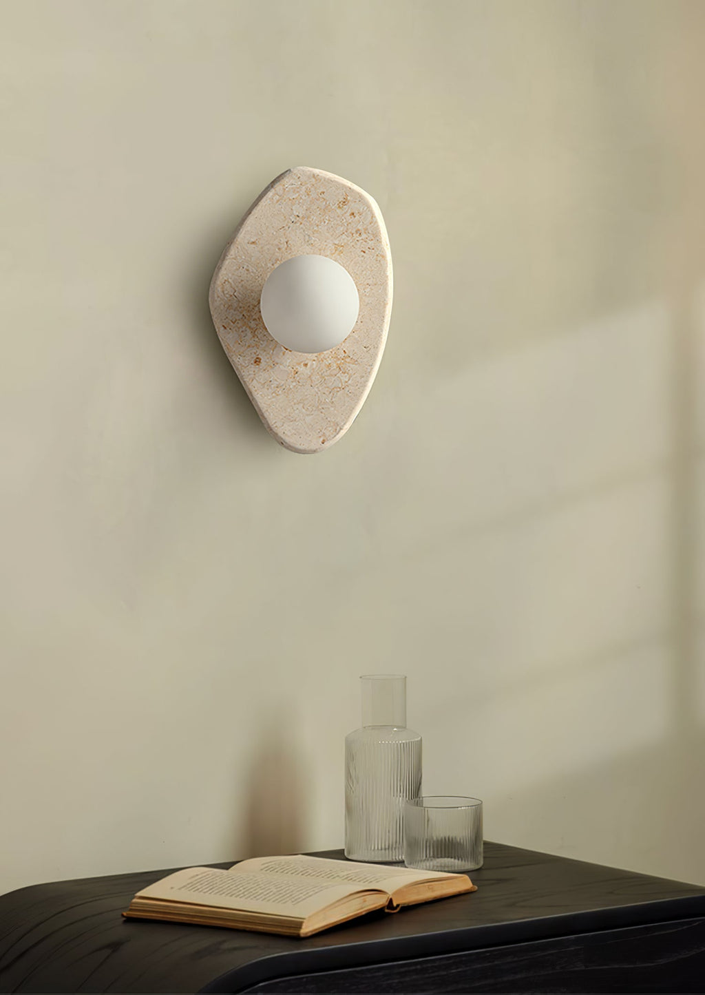 This Clérachic wall light glows above a dark bedside bench holding a vase, a glass and an open book.