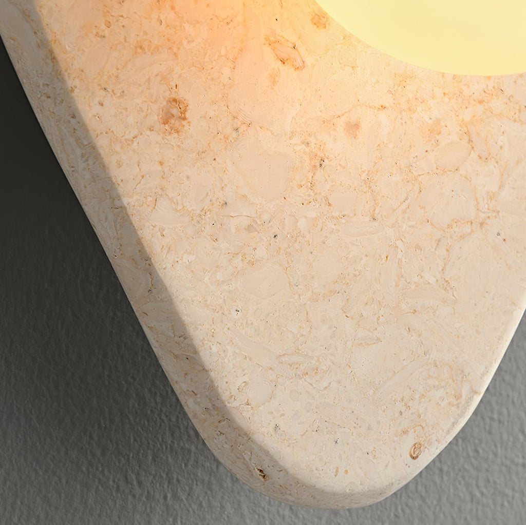 Close-up of the beige stone's rounded edge and mottled texture on this unlit Clérachic wall light.