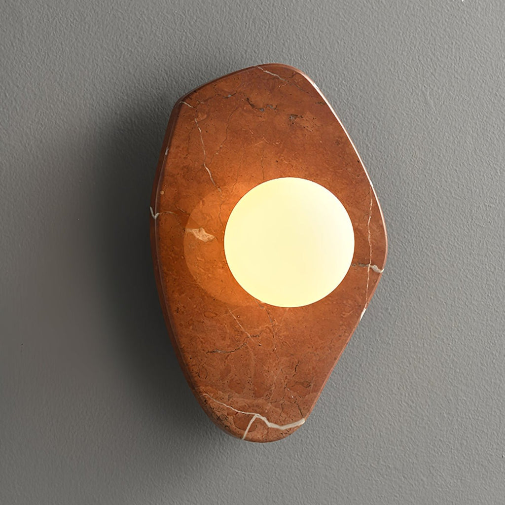 The coral-red marble version of this Clérachic wall light, glowing on a plain grey studio wall.