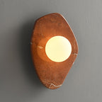 The coral-red marble version of this Clérachic wall light, glowing on a plain grey studio wall.