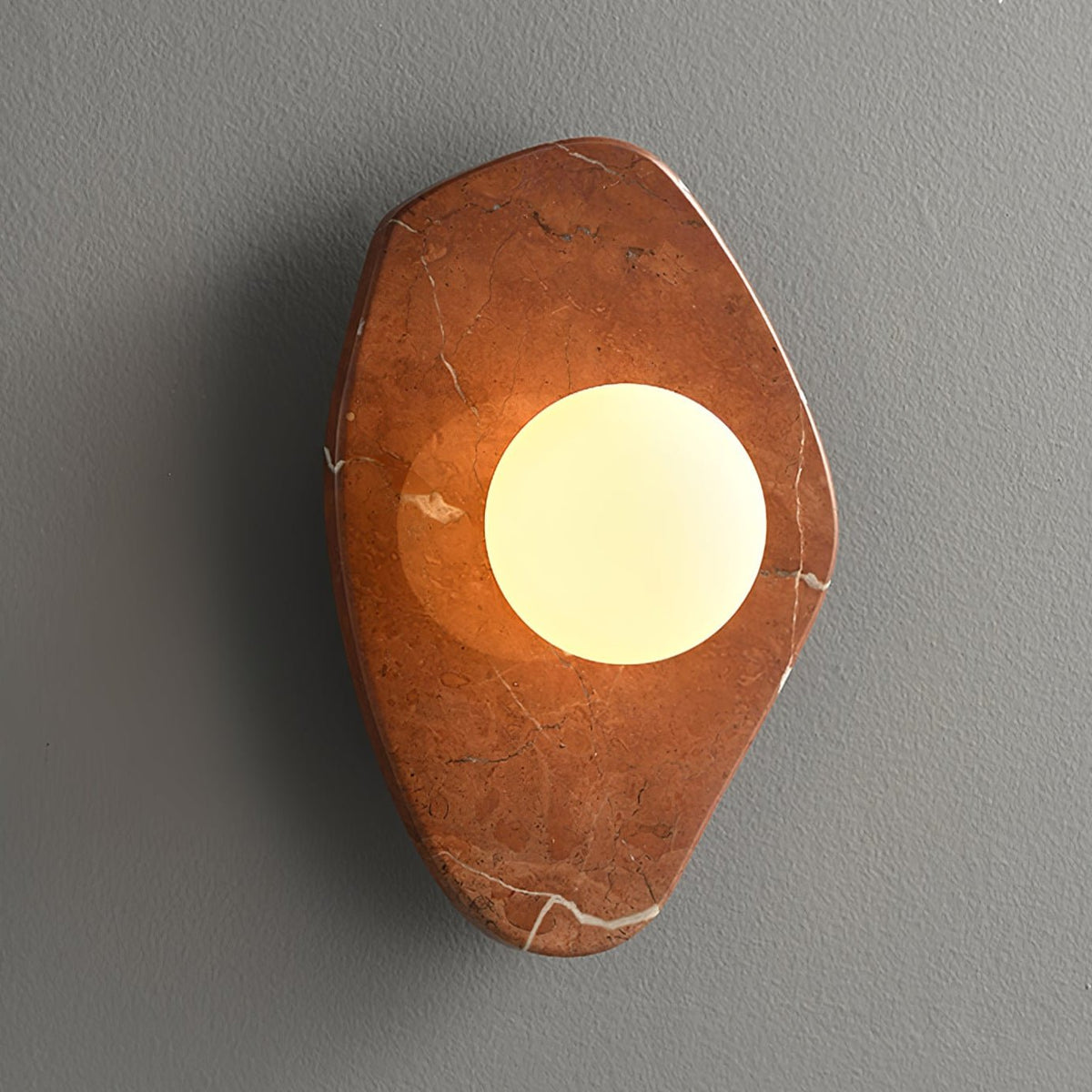 The coral-red marble version of this Clérachic wall light, glowing on a plain grey studio wall.