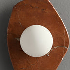 Top-down view of the coral-red marble wall light from Clérachic, centring the lit glass orb within the veined slab.