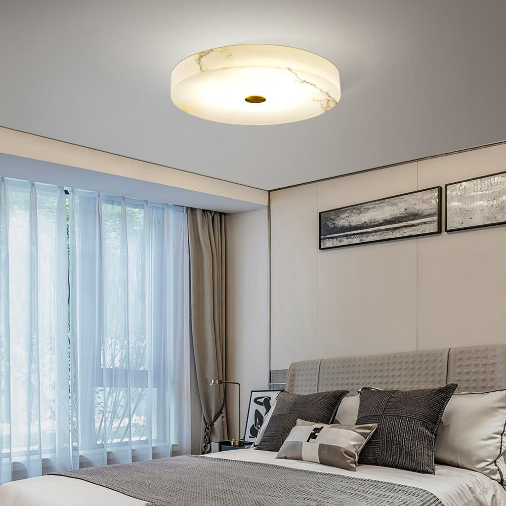 The Olaean flush mount lit in a bedroom, sheer curtains and a quilted headboard below.