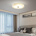 The Olaean flush mount lit in a bedroom, sheer curtains and a quilted headboard below.