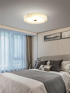 Olaean flush mount lit in a bedroom by a curtained window, veining in the alabaster clearly visible.