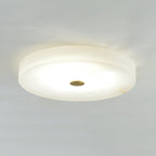 The Olaean flush mount lit and shot wide, brass cap set into the softly glowing alabaster underside.