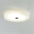 Olaean alabaster flush mount glowing on a pale ceiling, dark cap at the centre of the round diffuser.