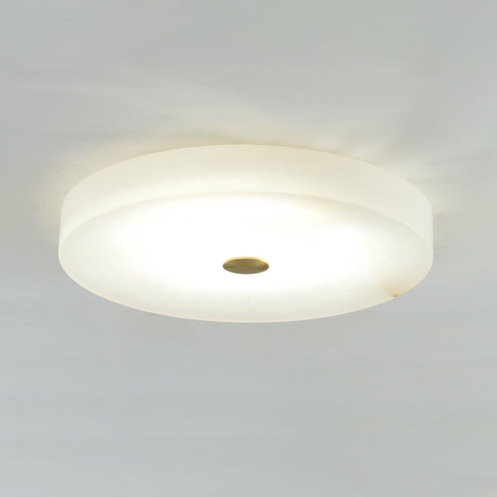 Lit Olaean flush mount viewed slightly off-centre, brass cap and smooth alabaster edge in frame.