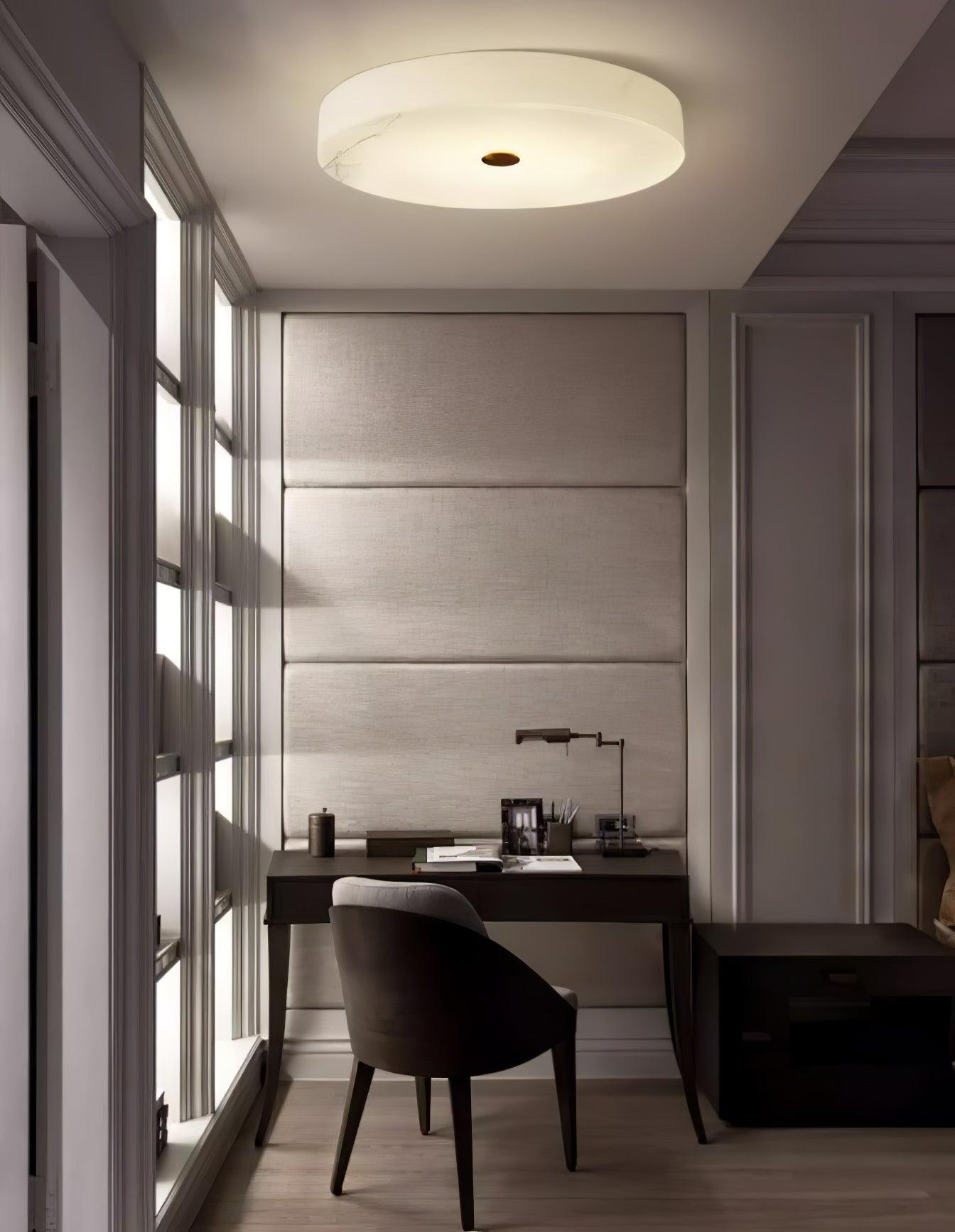 Olaean flush mount lighting a small study, glowing above a dark desk and upholstered wall panel.