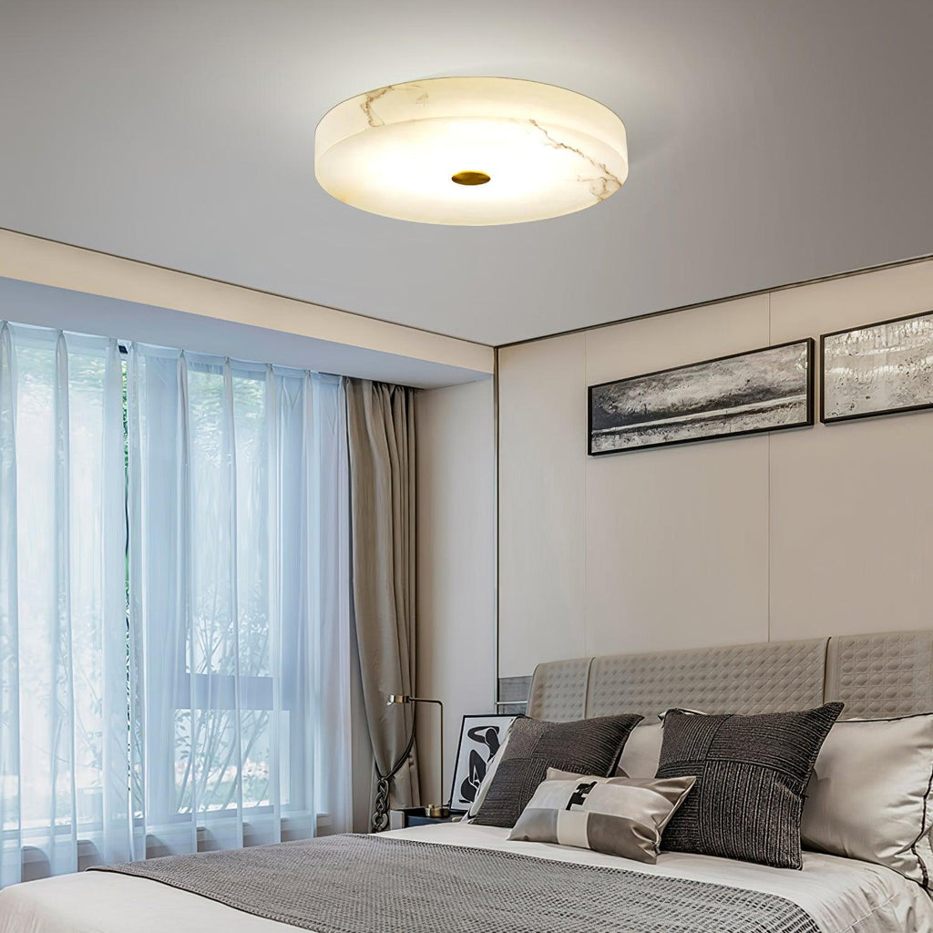 Square view of the Olaean flush mount lit above a bedroom, framed prints on the wall behind.