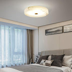Square view of the Olaean flush mount lit above a bedroom, framed prints on the wall behind.