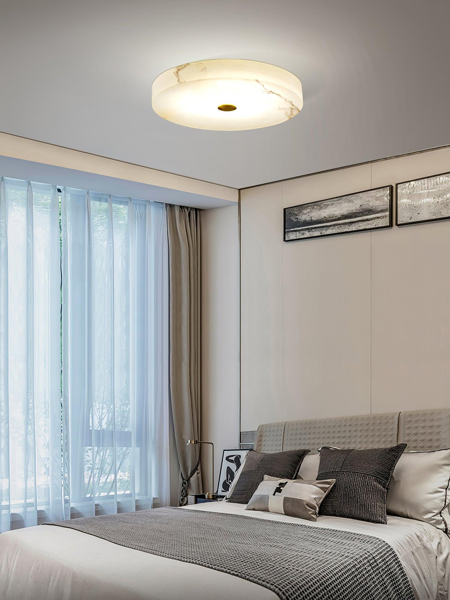 The Olaean flush mount seen from across a bedroom, its alabaster drum lit against a white ceiling.