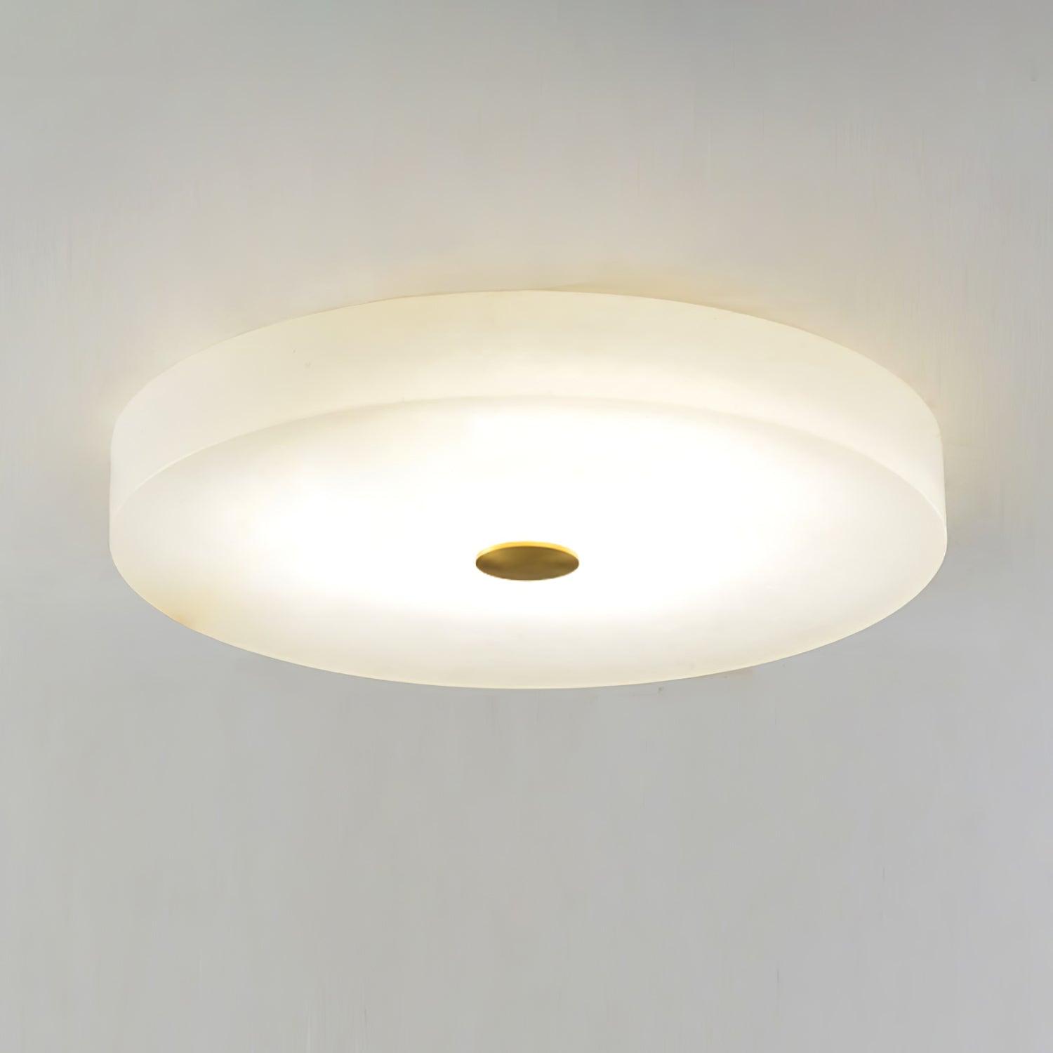 Olaean flush mount lit from within, the brass cap and stepped alabaster rim seen close from below.