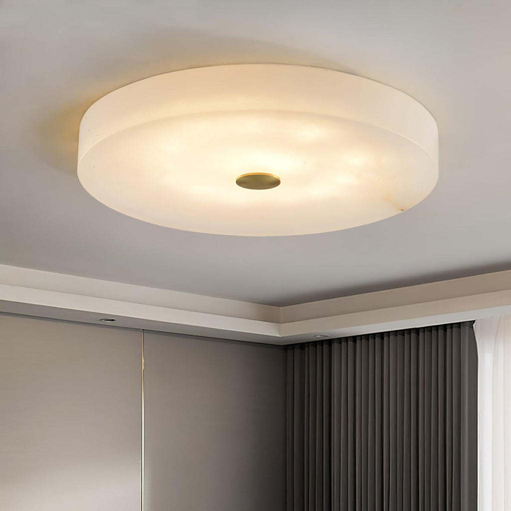 Large Olaean flush mount lit in a room corner, brass cap centred beneath the wide alabaster drum.