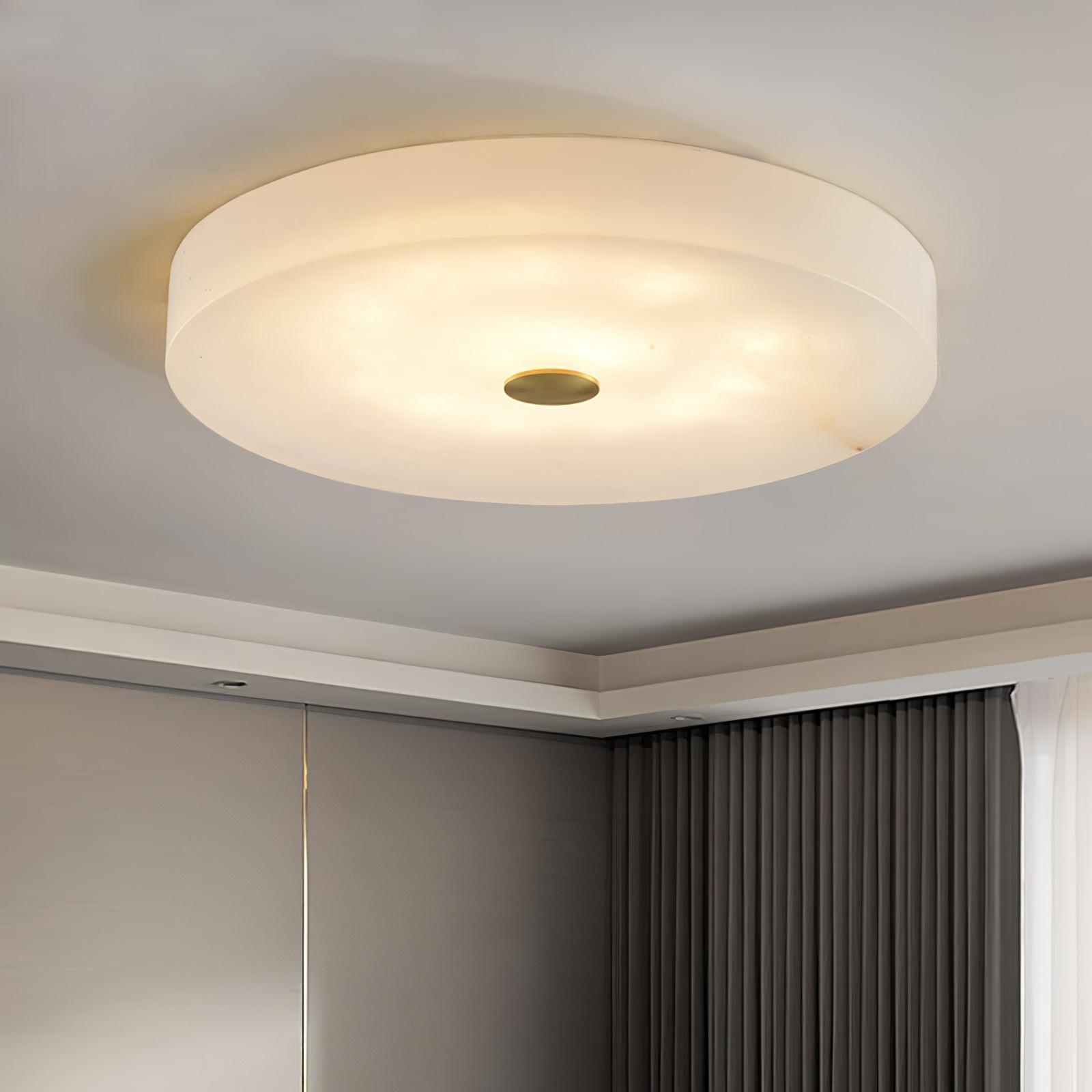 Large Olaean flush mount lit in a room corner, brass cap centred beneath the wide alabaster drum.