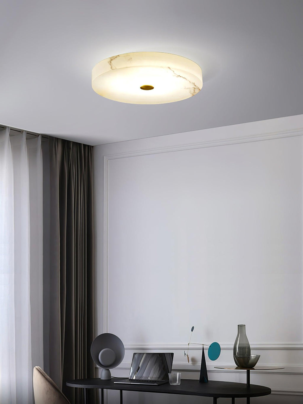 Olaean flush mount glowing above a work corner with a laptop, vase and dark curtains.